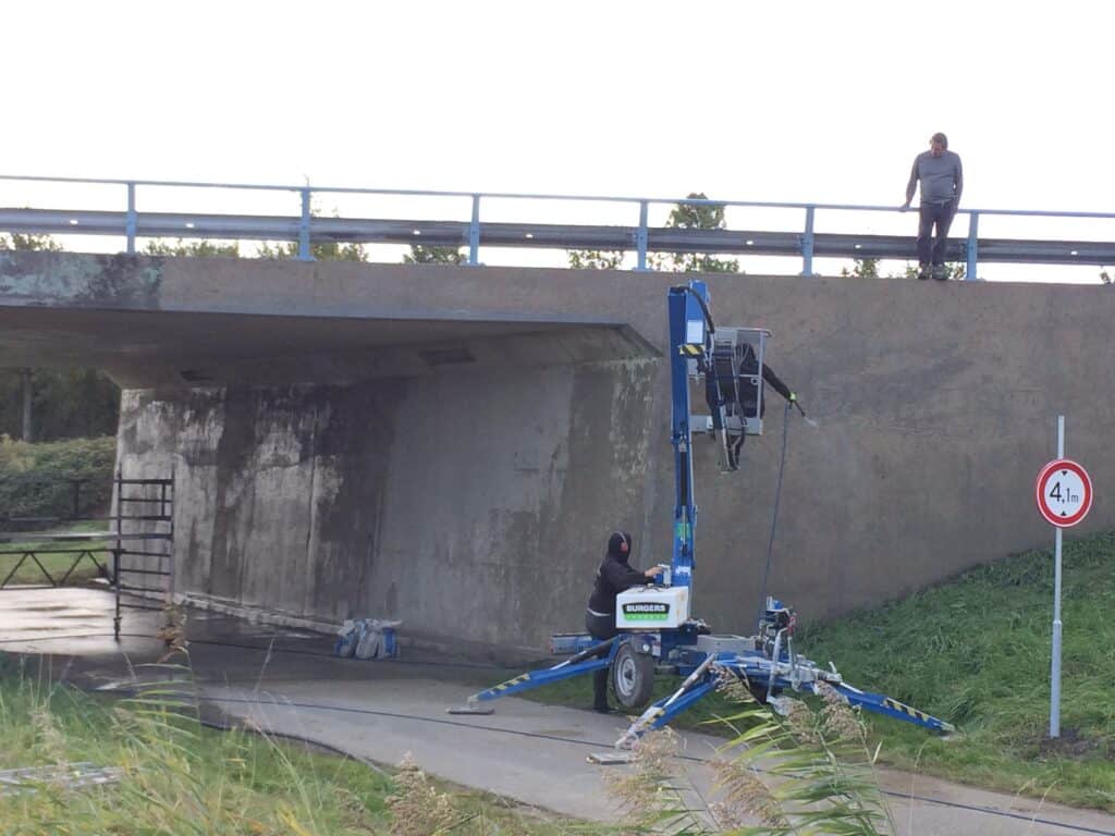 Vakman werkt vanuit een hoogwerker aan graffiti verwijderen zonder schade aan het viaduct